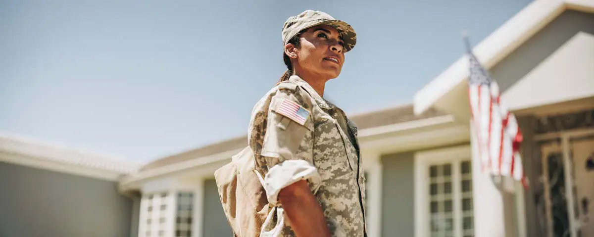 U.S. Army veteran in uniform outside a home with an American flag